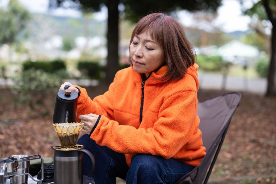 Woman in orange fleece pouring coffee into a cup, in the nature