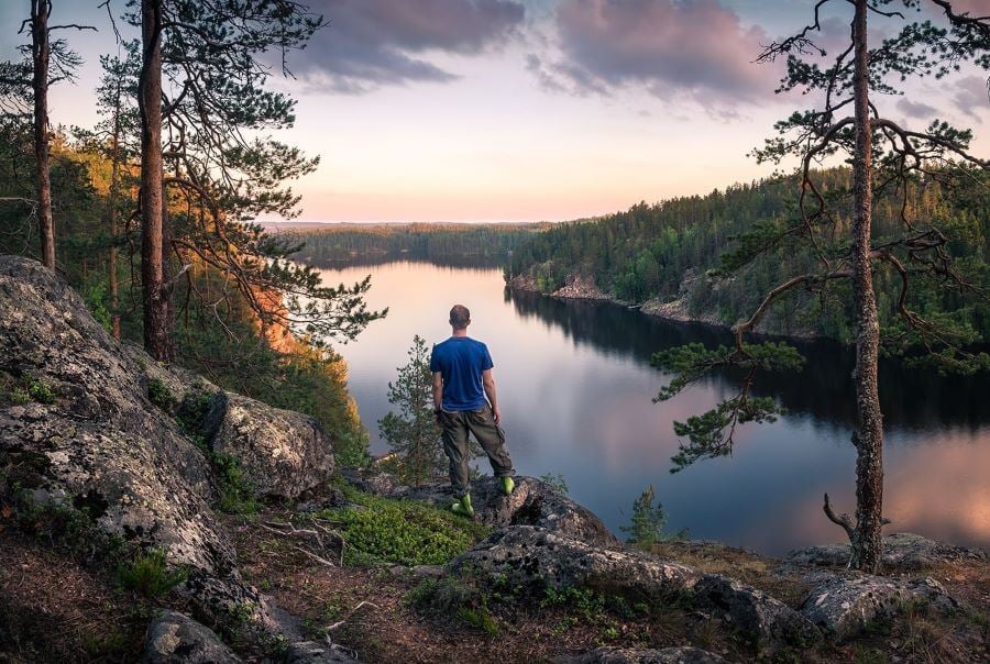 Man standing on a cliff in the forest looking out over a lake